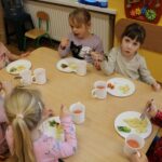 Dzieci przy stolikach jedzą obiad