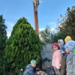 3. Dzieci układają kwiaty i znicze pod krzyżem na cmentarzu w Krzydłowicach