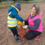 Chłopiec wsypuje ziemniaki do worka siatkowego trzymanego przez Panią Ewę
