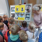 Katechetka rozmawia z dziećmi przed tablicą ze zdjęciami papieża