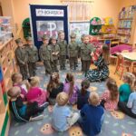 Dzieci ubrane w ubrania żołnierskie, nauczycielka prezentuje im symbole narodowe