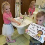Dziewczynka myje dłonie, chłopiec trzyma ilustracje dotyczącą mycia rąk