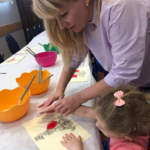 Nauczycielka pomaga dziecku zrobić odcis dłoni na kartce