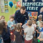 dzieci wręczają policjantowi upominek za przekazanie cennych informacji na temat bezpiecznych ferii