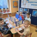Dzieci przy stolikach z własnoręcznie zrobionymi komputerami z papieru