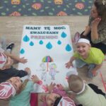 Dzieci wykonuja pracę plastyczną grupową z odbijaniem rączek w farbie