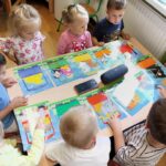 Przedszkolaki przy stoliku oglądają ilustracje do słuchowiska