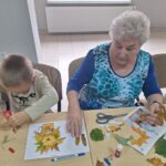 dzieci wraz z seniorami przyklejają liście