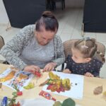 dzieci wraz z seniorami przyklejają liście