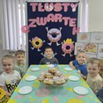 Chłopcy z oddziału Krasnoludki siedzą przy stoliku z pączkami