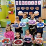 Dzieci trzymają w ręce swoje prace plastyczne przy tablicy tematycznej