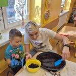 Dziecko przy pomocy pani sadzi kwiata