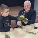 dzieci wraz z seniorami wykonują wielkanocne palmy