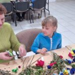 dzieci wraz z seniorami wykonują wielkanocne palmy