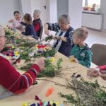dzieci wraz z seniorami wykonują wielkanocne palmy