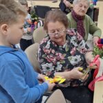 dzieci wraz z seniorami wykonują wielkanocne palmy