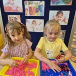 Dziewczynki za pomocą formy wycianją kształty z piasku kinetycznego