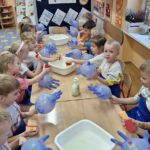 Dzieci przy stolikach, mycie wodą rekawiczek ubrudzonych farbą