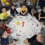 Dzieci siedzą w kole i bawią się eliksirami z zadaniami