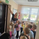 Pani Ewa pokazuje dzieciom z oddziału Tulipanki znak wyjścia ewakuacyjnego nad drzwiami w przedszkolu.
